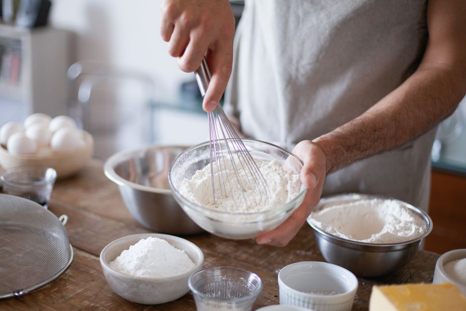 Chef's hands whisking flour in a bowl, surrounded by baking ingredients.