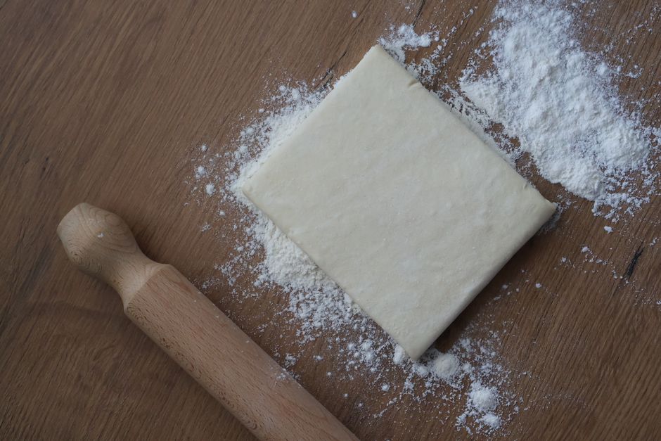 Top view of a dough block with flour and rolling pin on a wooden table.