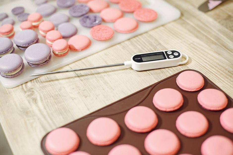 From above of colored macaroon shells placed on wooden table in pastry store with cooking thermometer